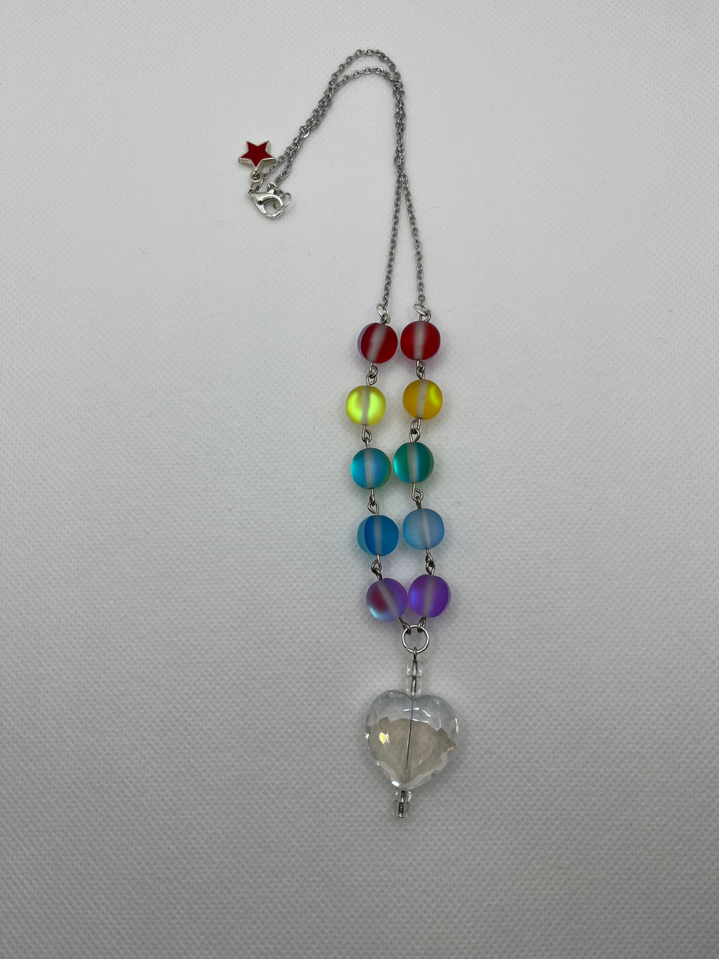 Rainbow reflective beaded necklace with a clear heart-shaped pendant laid flat against a white background.