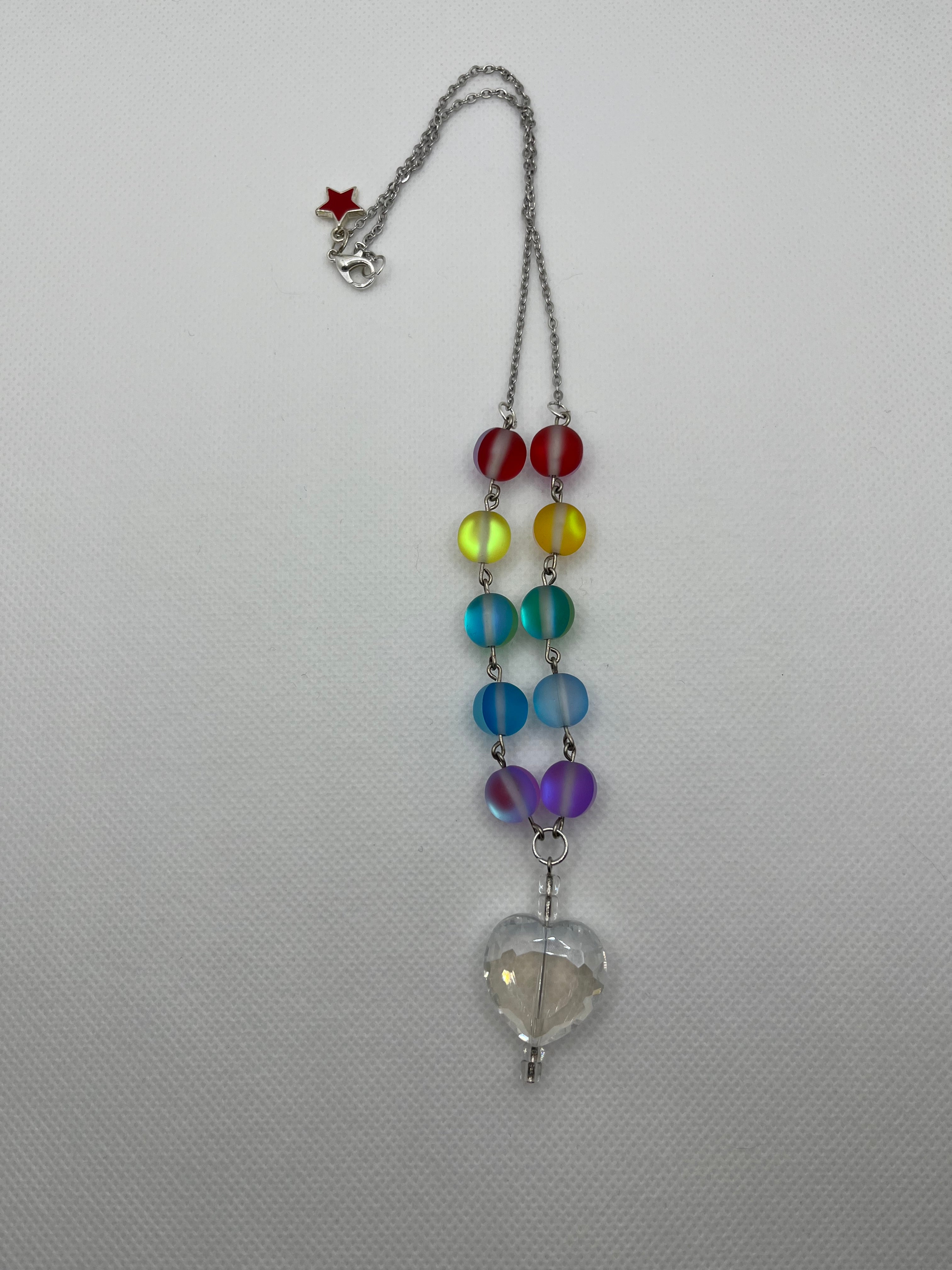 Rainbow reflective beaded necklace with a clear heart-shaped pendant laid flat against a white background.