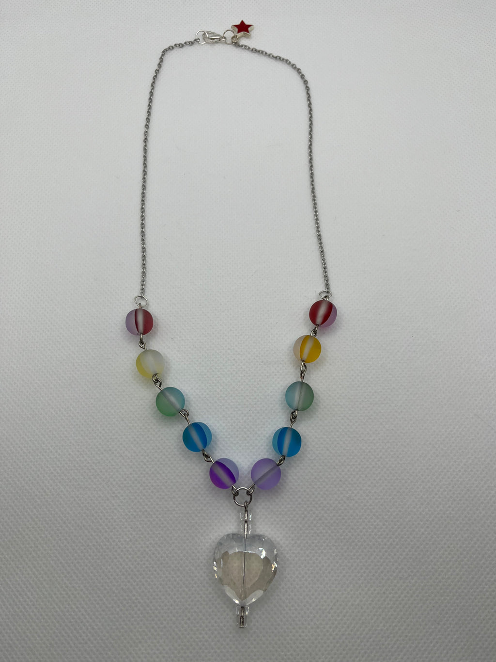 Rainbow reflective beaded necklace with a clear heart-shaped pendant laid flat against a white background.