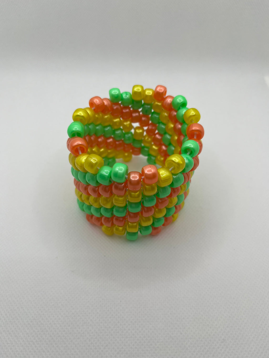 Orange, yellow, and green spiral beaded cuff bracelet against a white background