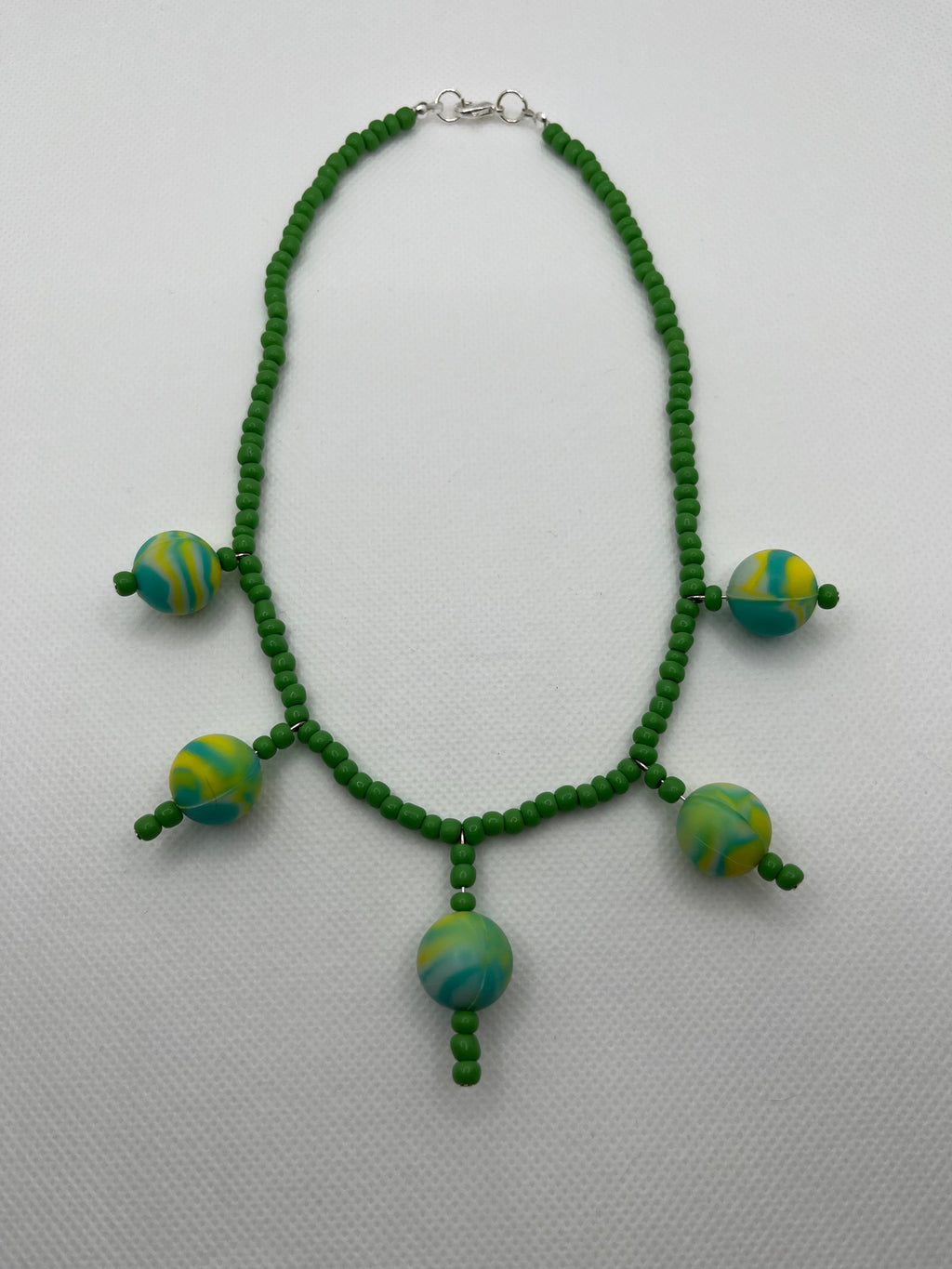 Green seed bead necklace with silicone beads strung throughout laid flat against a white background.