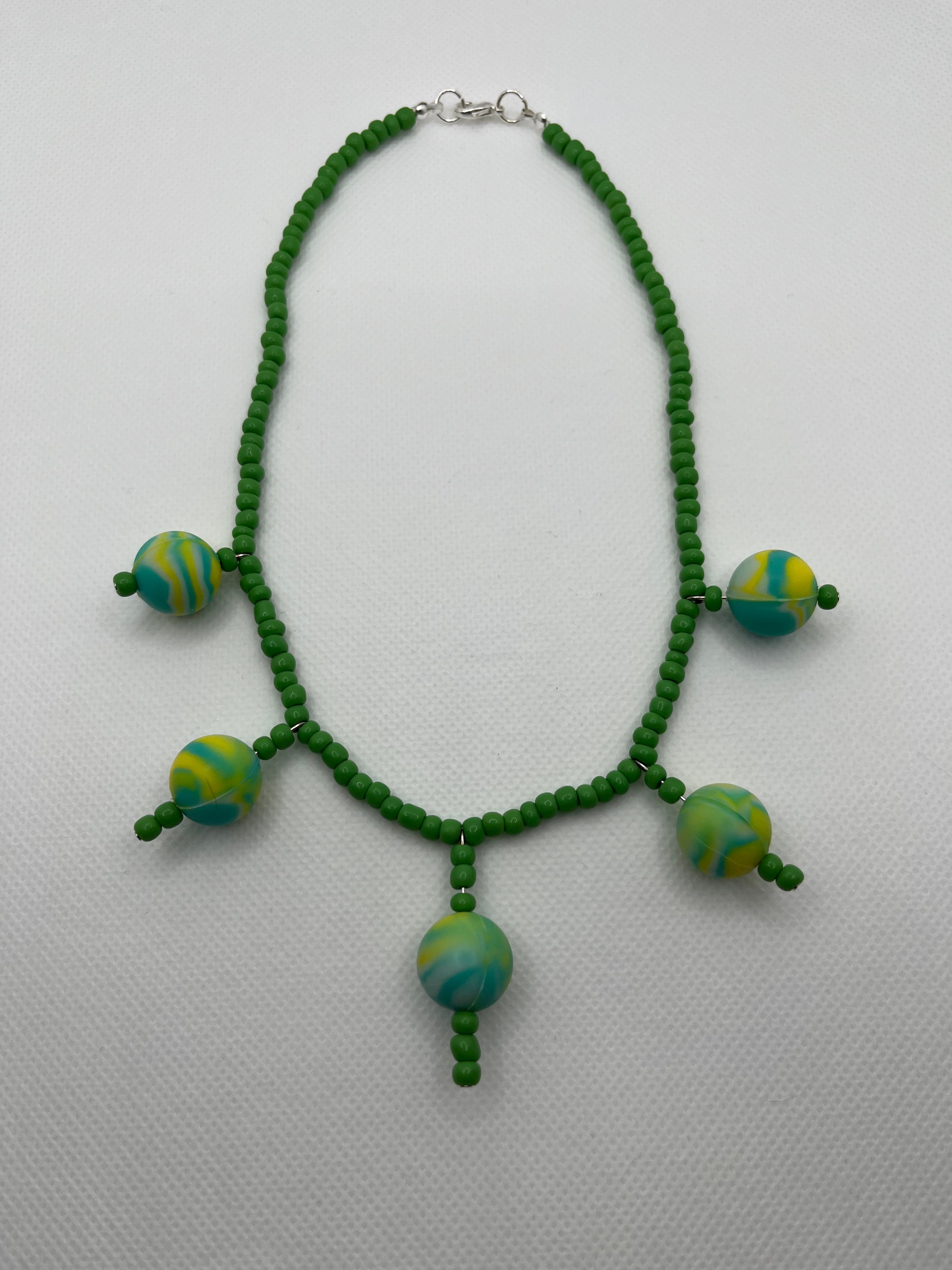 Green seed bead necklace with silicone beads strung throughout laid flat against a white background.