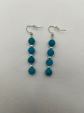 Four blue beads with silver spacer beads on silver earrings against a white background