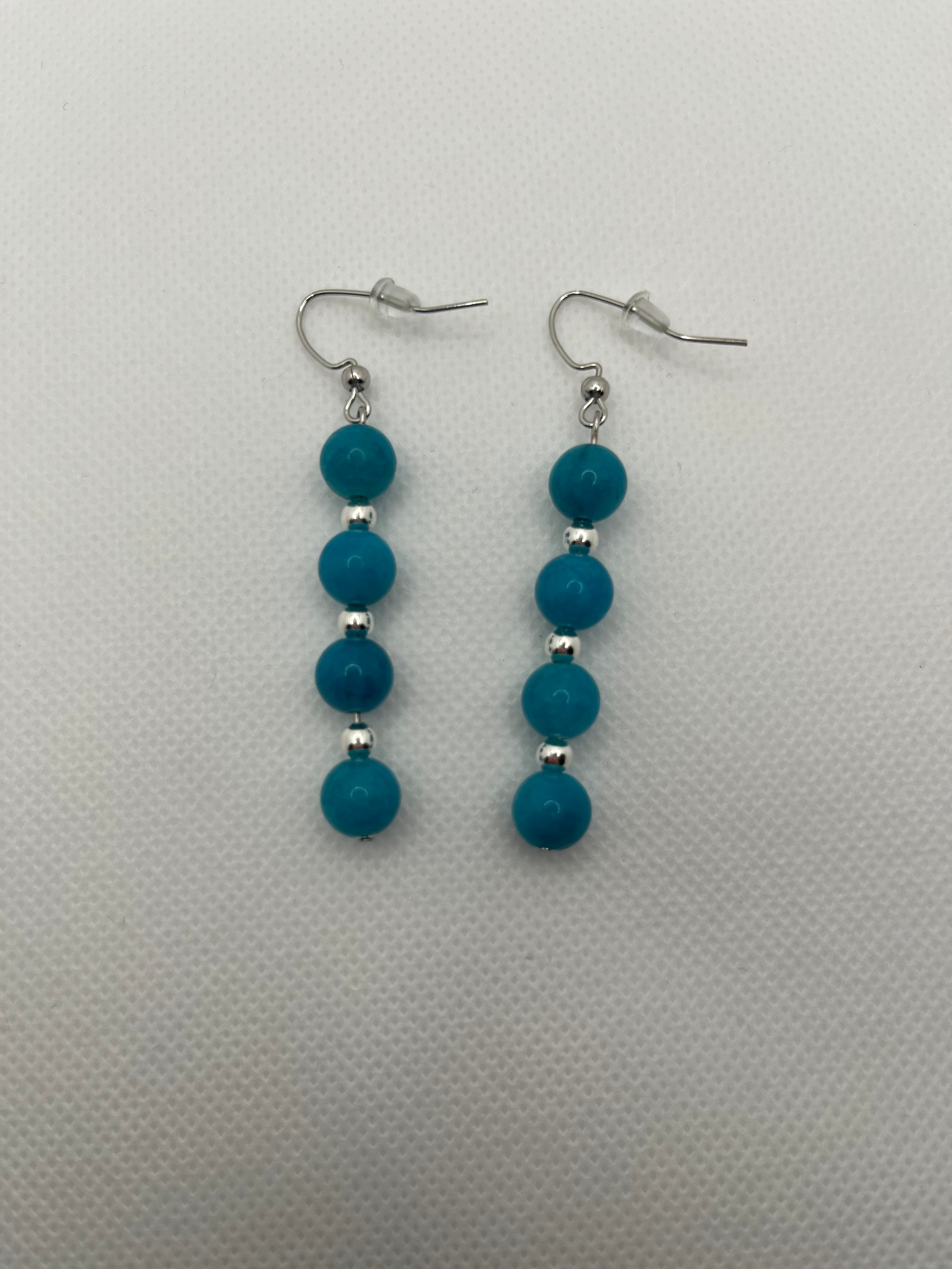 Four blue beads with silver spacer beads on silver earrings against a white background
