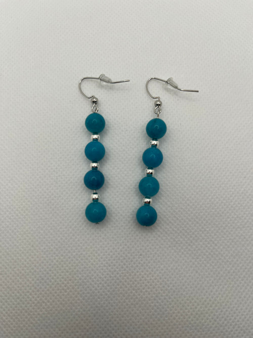 Four blue beads with silver spacer beads on silver earrings against a white background