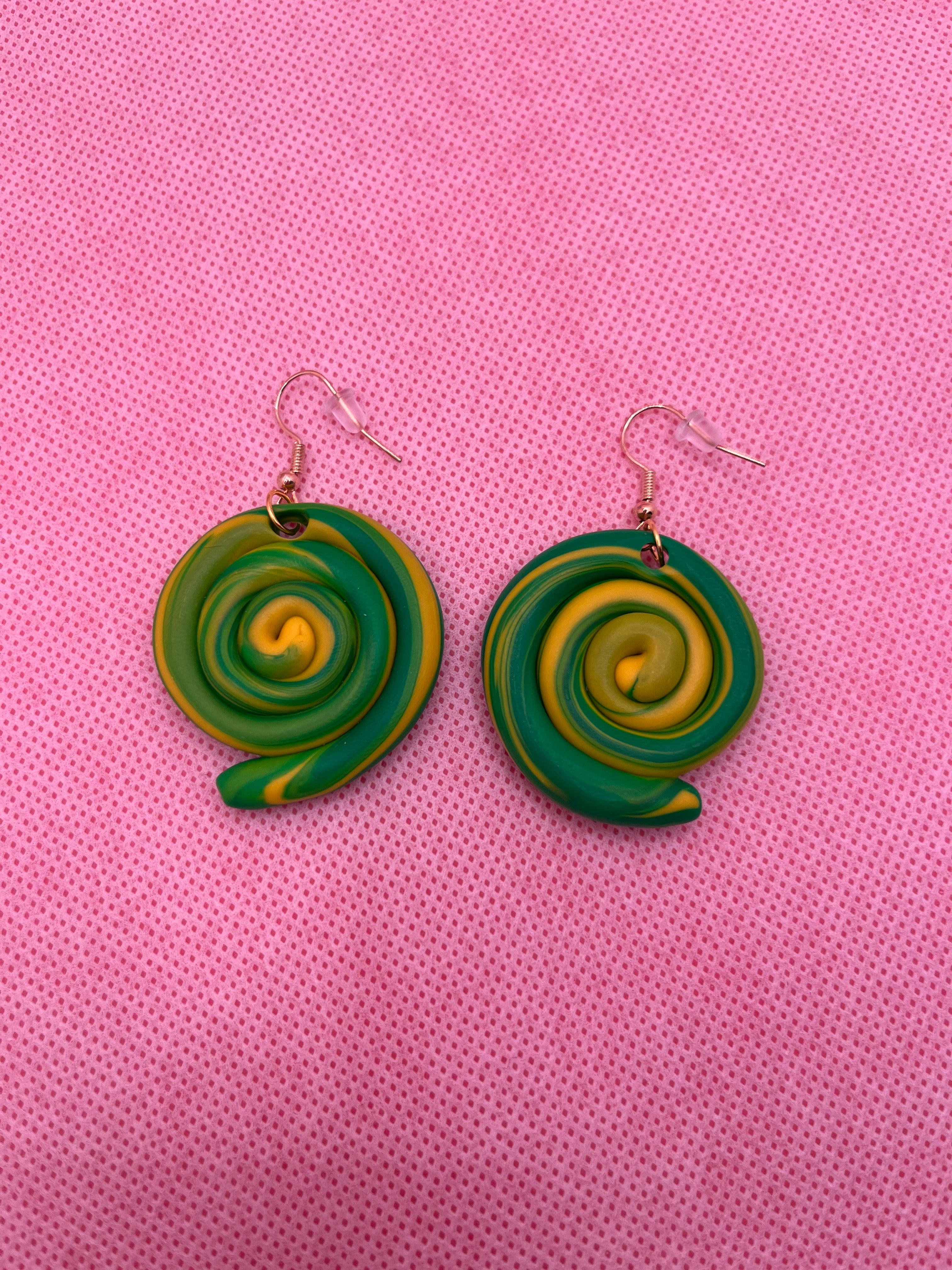 Green and yellow circle swirl earrings against a pink background