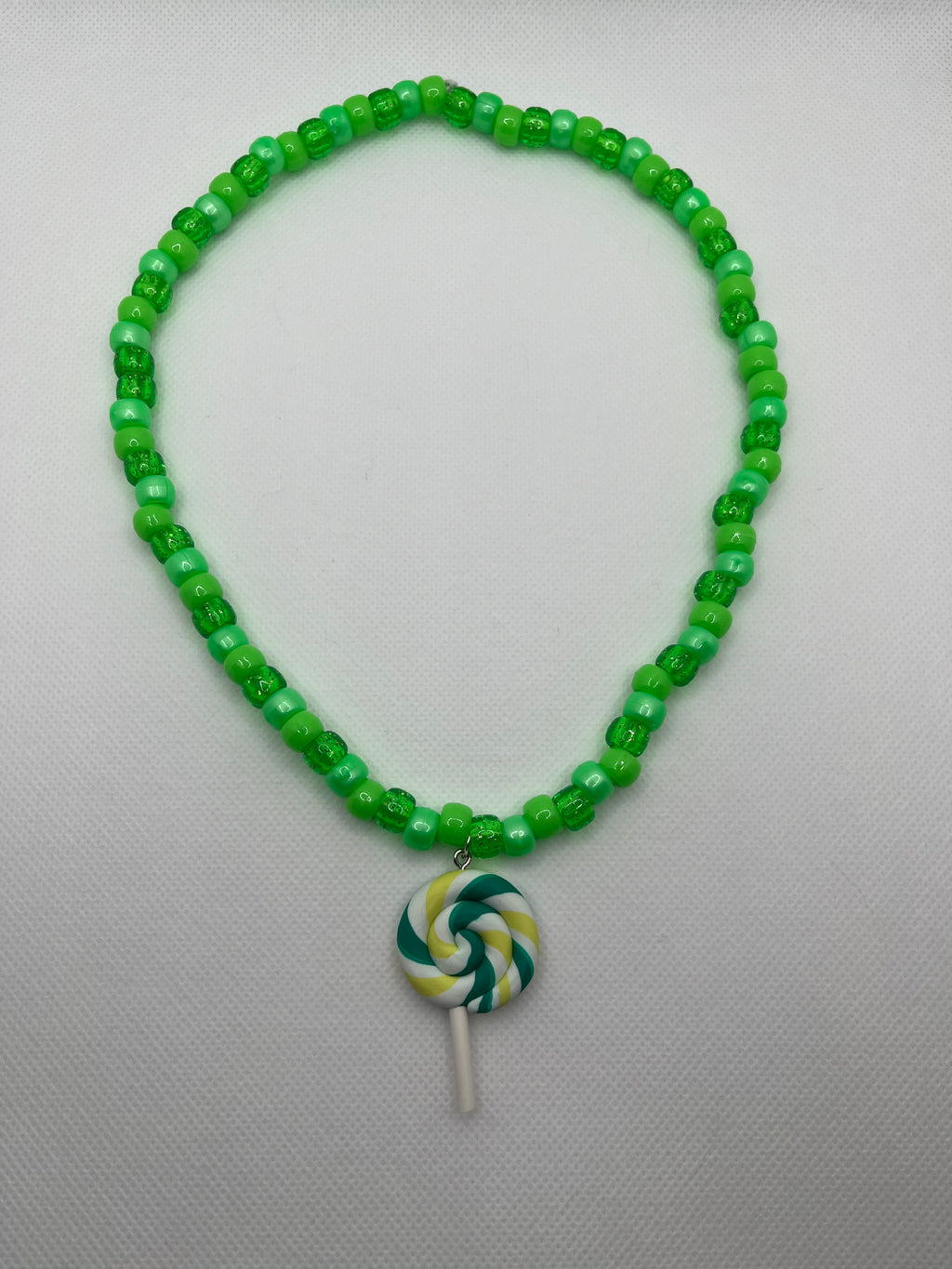 Green beaded necklace with green lollipop pendant on a white background