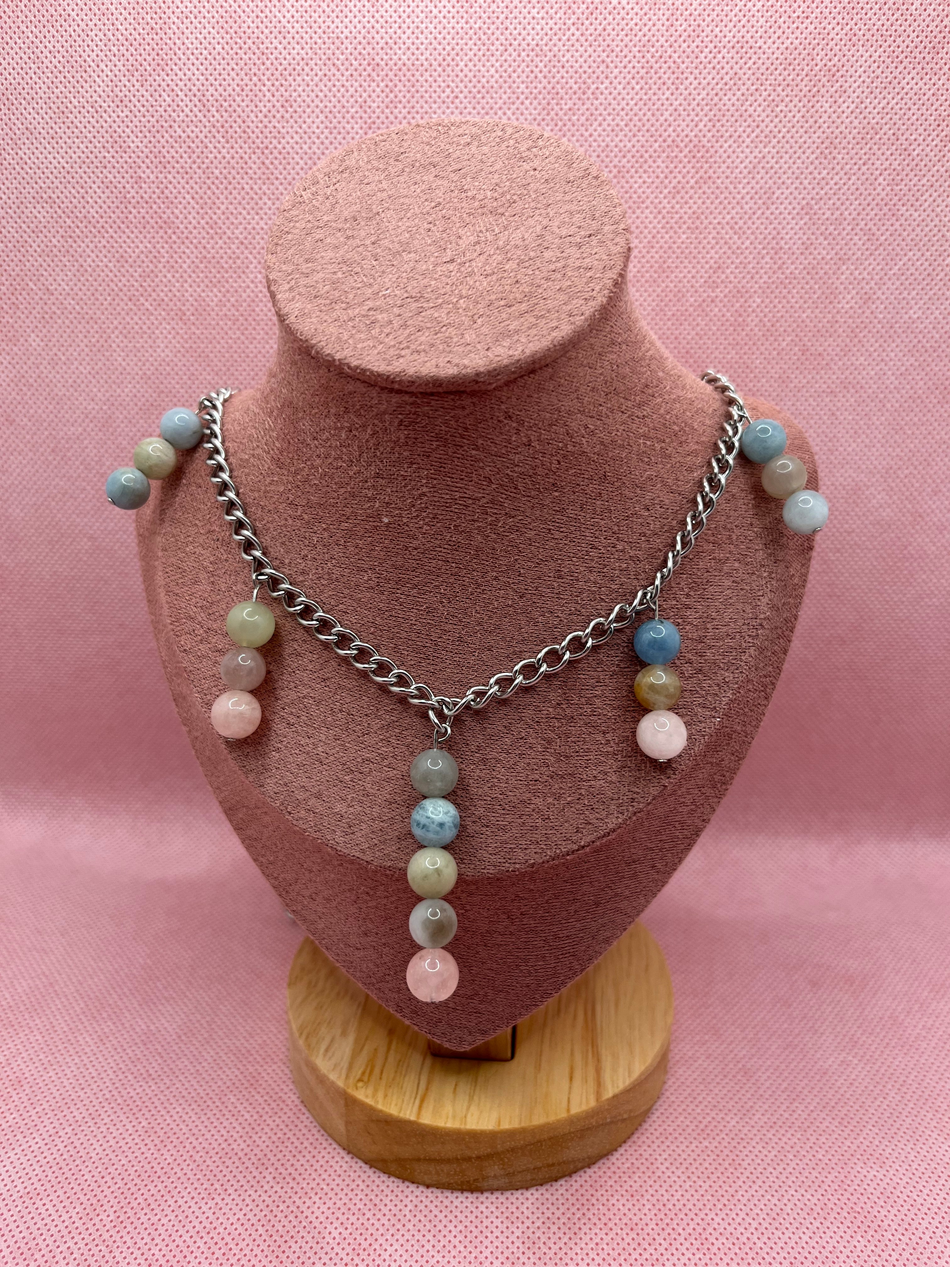 Necklace with multi-bead pastel pendants throughout draped over a blush pink mannequin with a pink background.