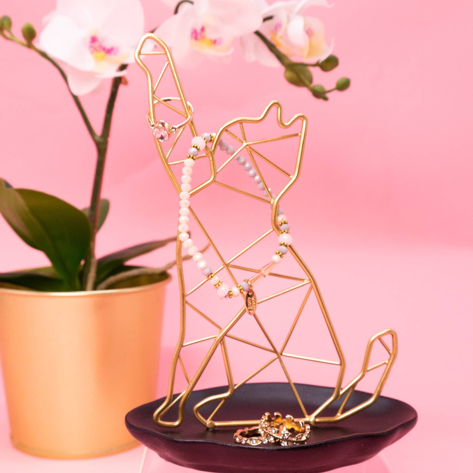 Gold geometric cat shaped jewelry holder with jewelry on a pink background