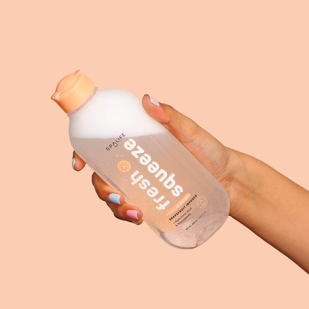 Hand holding a bottle of 'Fresh Squeeze' micellar water against a beige background