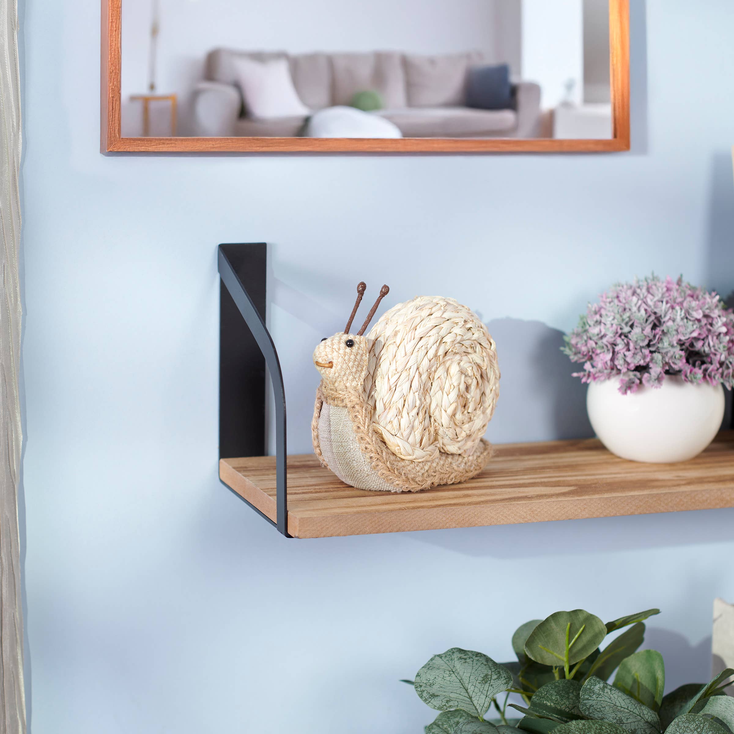 Wooden shelf with decorative items including a knitted snail and a small plant, against a light blue wall.